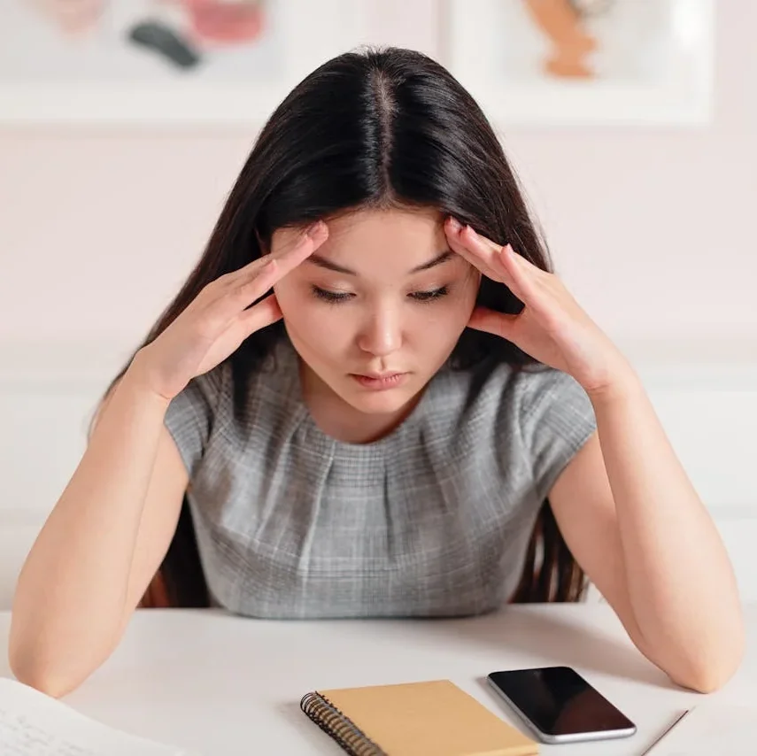 Woman sitting at desk with hands on head